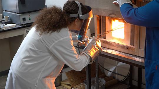 Woman retrieving melted glass from a furnace